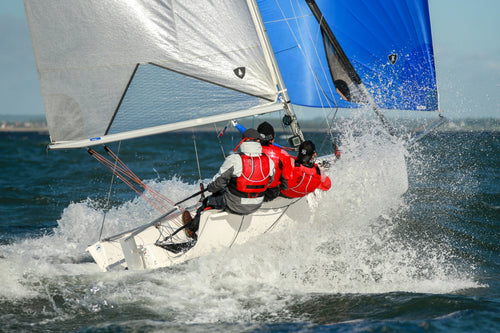 Sailors on a racing sailboat cutting through waves under blue and white sails