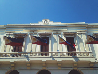 Philippine flags on the Bureau of the Treasury building in Manila. Photo: RJ Joquico / Unsplash. Illustrative heritage imagery, not the Aguinaldo Shrine.