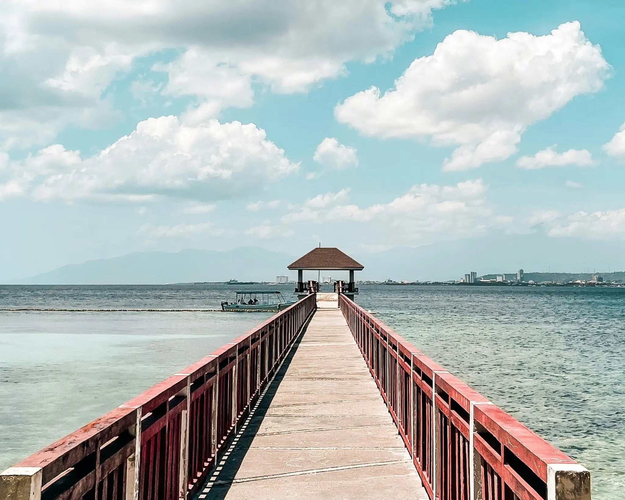 A long pier extending over bright coastal water beneath wide clouds