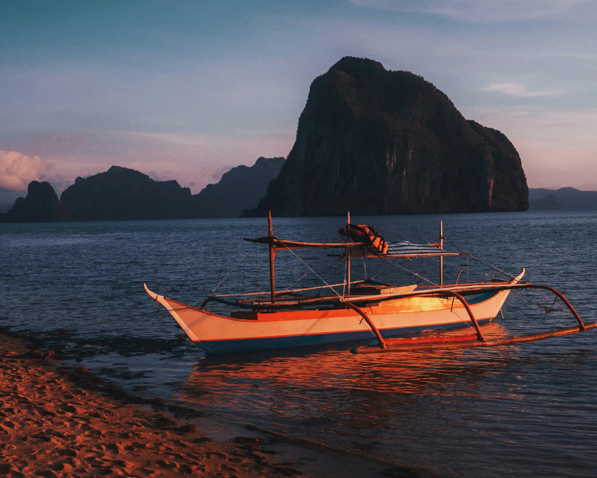 A traditional outrigger boat resting beside limestone islands at sunset in Palawan
