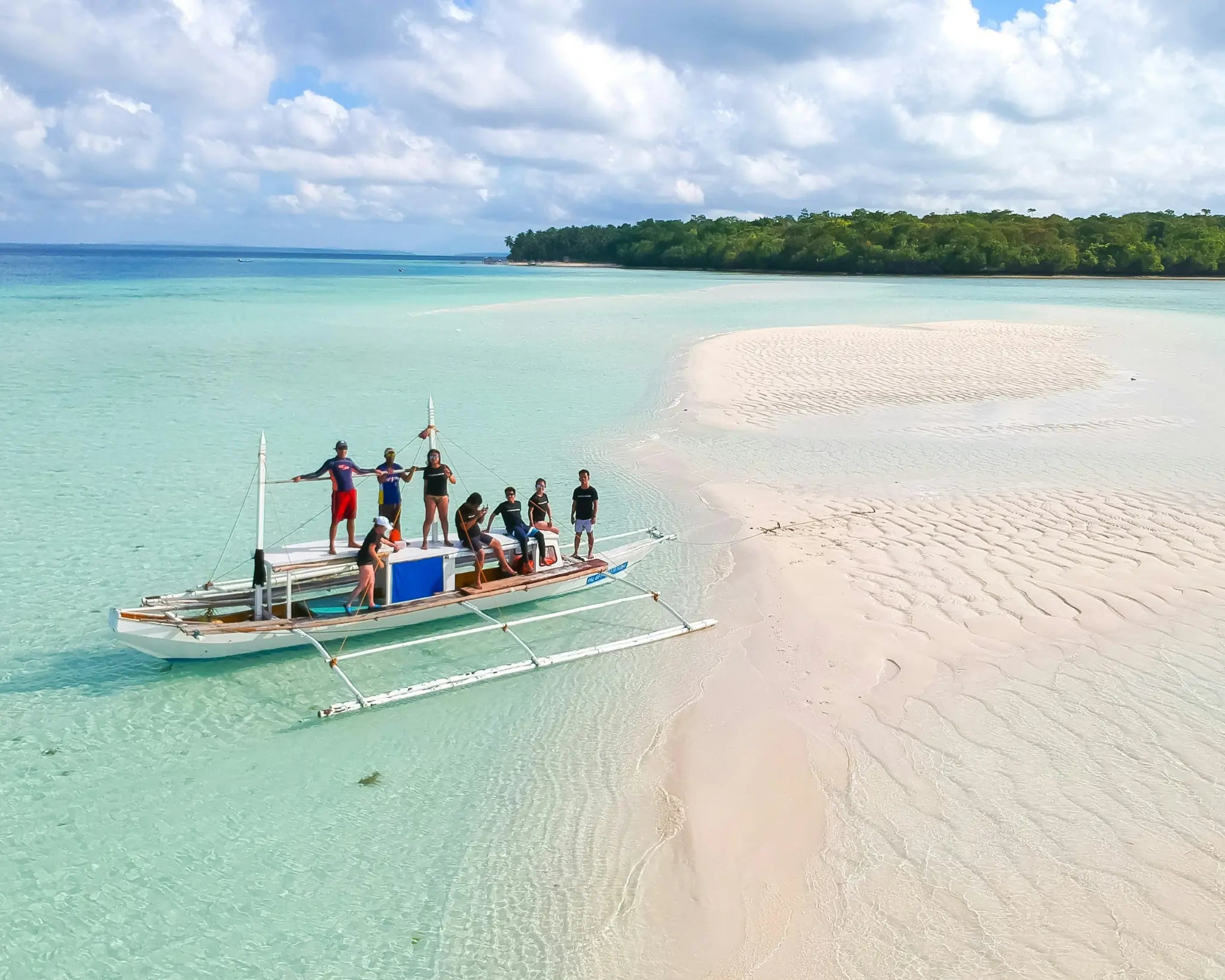 A group arriving by traditional outrigger boat at a tropical sandbar